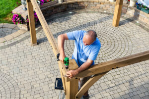 man,building,a,wooden,gazebo,on,a,brick,patio,with